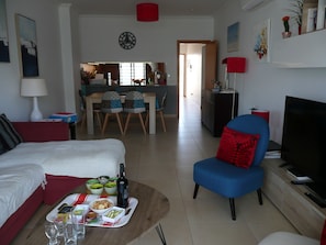 Un salon avec un canapé, un coin repas avec des chaises, un téléviseur et une cuisine à l’arrière-plan.