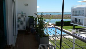 En balkon med havudsigt, en pool og en hvid bygning over vandet.