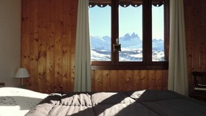 Un dormitorio con pared de madera, una cama, un ventanal con vista a la montaña y una lámpara.