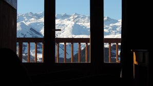 Una habitación con vista a montañas nevadas a través de una ventana con barandilla de madera.