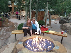 Two people sitting on a bench with a fire pit in front of them.