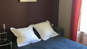 A neatly made bed with white pillows and a blue bedspread in a room with a dark wall, a framed picture, and a red curtain. - Guest room  for 2 persons in Douarnenez bay  (Plonévez-Porzay)