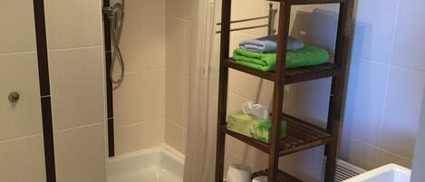 A small bathroom with a shower, a toilet, and a shelf with towels and toiletries.
