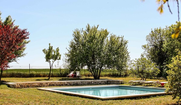 Ein rechteckiger Swimmingpool, umgeben von einer Steinmauer, mit Rasen und Bäumen im Hintergrund.