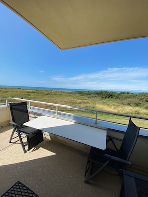 A balcony with a table and two chairs, overlooking a coastal landscape.