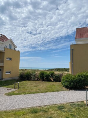 A residential area with two yellow buildings, a gravel path, and a grassy field with a view of the sea.