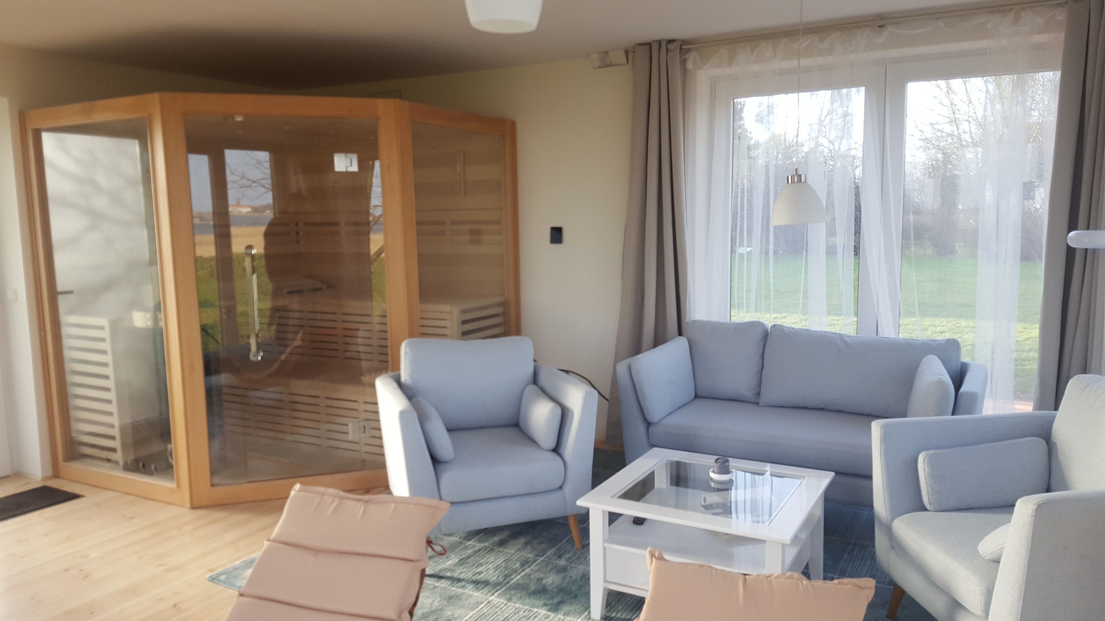 A modern living room with a grey sofa, two armchairs, and a glass coffee table. A sliding glass door leads to a patio area.