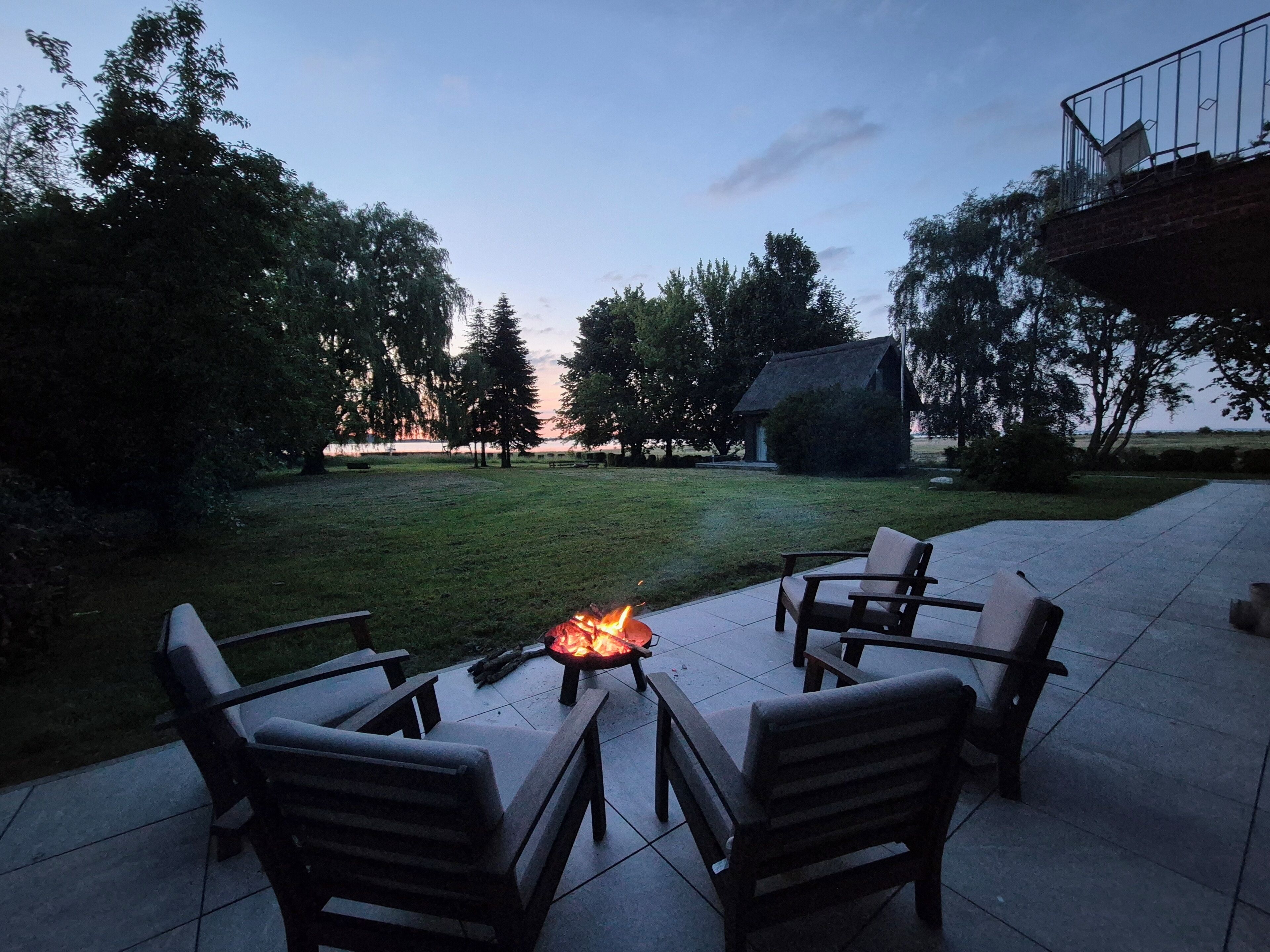 A patio with a fire pit, outdoor furniture, and a view of trees and a building.