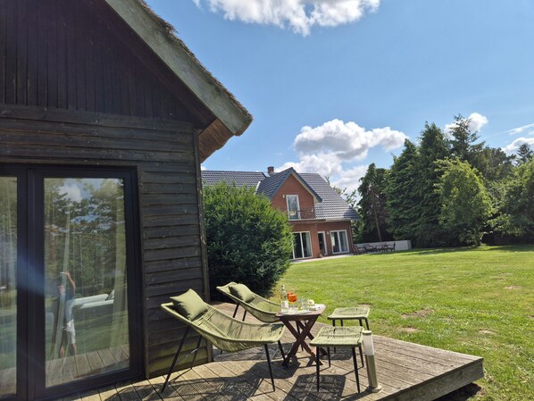 A wooden deck with outdoor furniture, a glass door leading to a room, and a house in the background.