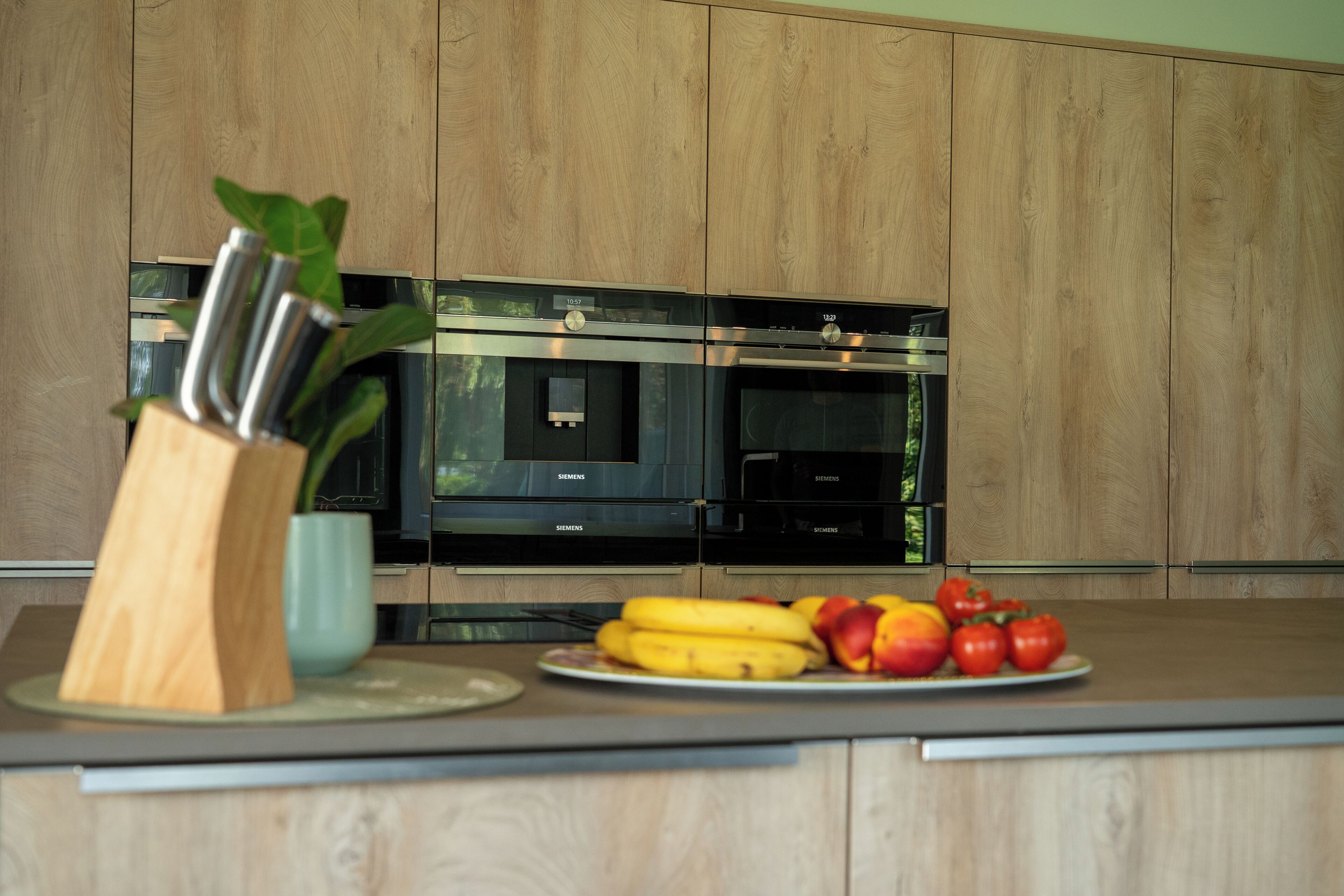 A modern kitchen with wooden cabinets, stainless steel appliances, and a fruit bowl on the counter.