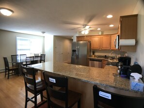 A kitchen with granite countertops, wooden cabinets, a stainless steel refrigerator, and a dishwasher.