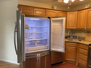 A stainless steel refrigerator with an open door, revealing its interior compartments.