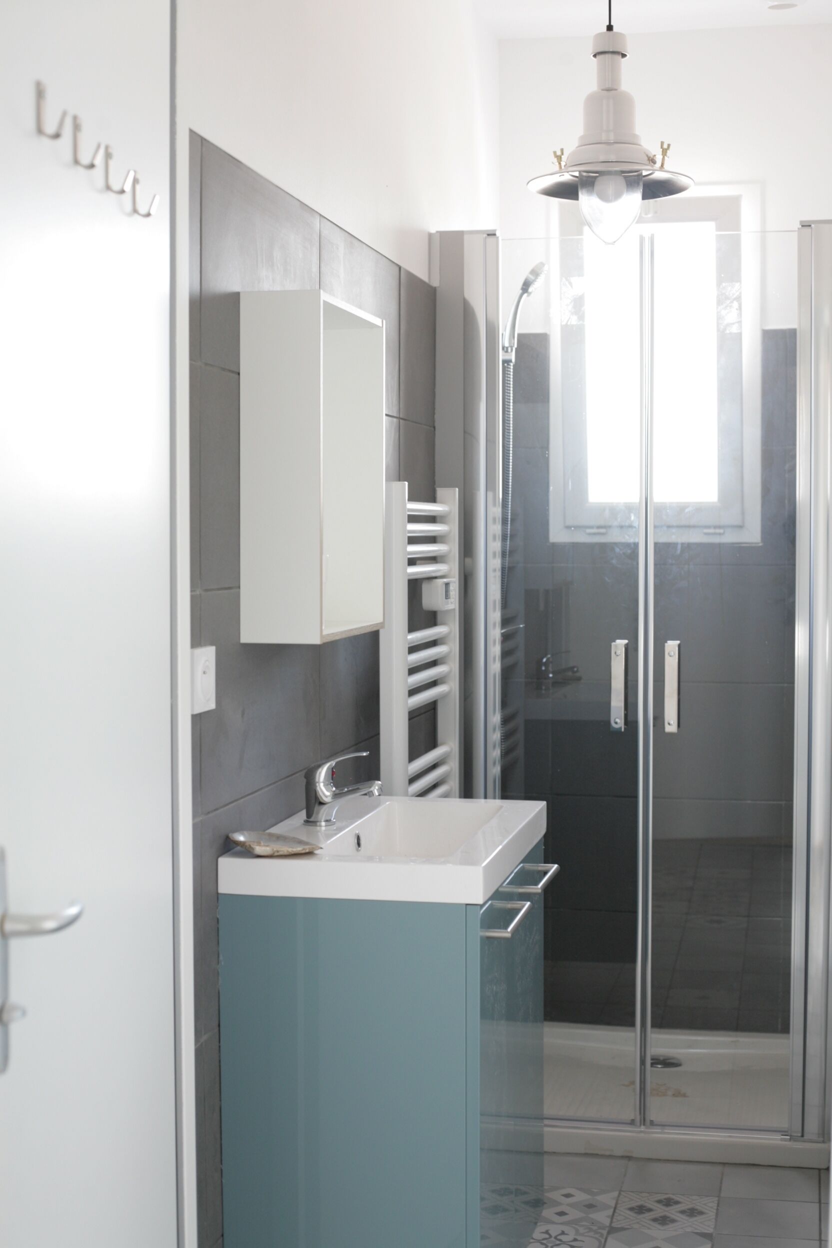 A modern bathroom with a glass shower enclosure, a white sink, and a blue cabinet.