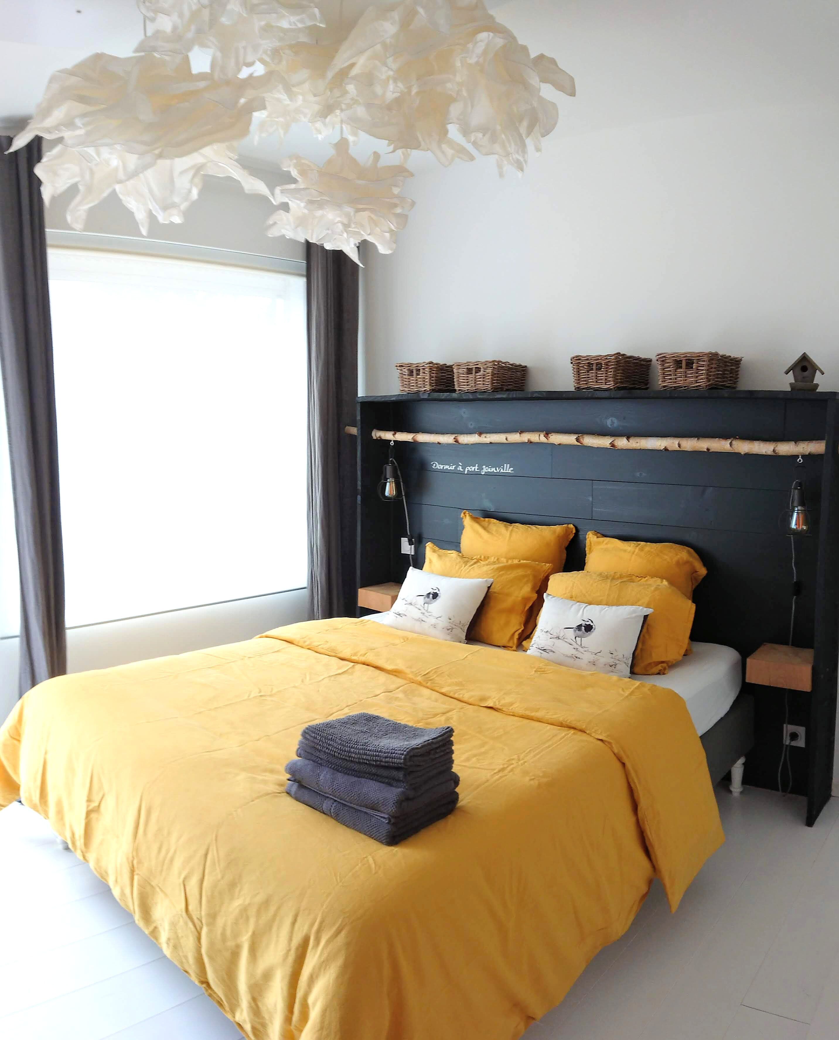 A bedroom with a bed, yellow bedding, a dark headboard, and a hanging light fixture.