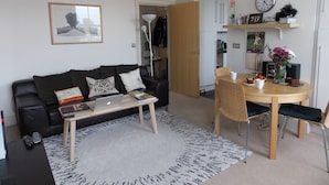 A modern living room with a black leather sofa, a wooden coffee table, and a dining area with a wooden table and chairs.