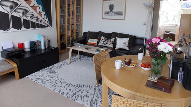 A living room with a sofa, a coffee table, a bookshelf, and a painting on the wall.