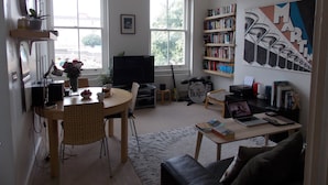 A living room with a dining table, chairs, a bookshelf, a television, and a guitar.