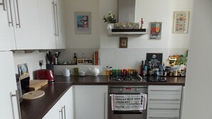 A compact kitchen with white cabinets, a wooden countertop, a red toaster, and a stainless steel oven.
