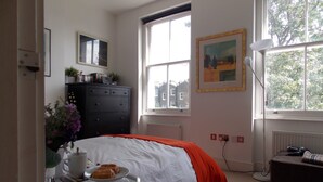 A bedroom with a bed, a dresser, a window, and a painting on the wall.