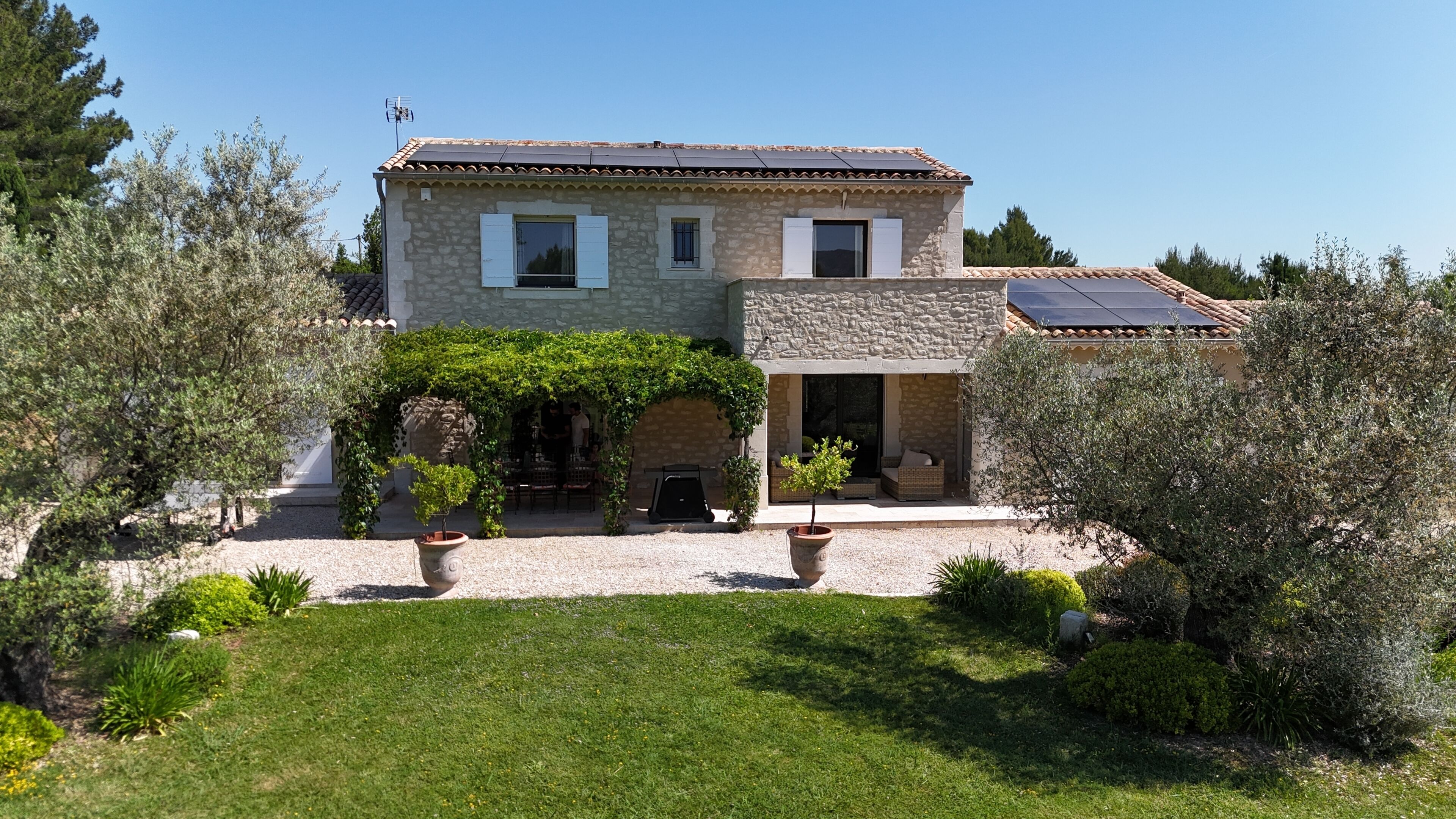 Une maison en pierre avec un jardin, une terrasse et un panneau solaire.