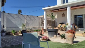 Un patio moderno con mobiliario exterior, plantas en macetas y una vista despejada del edificio contiguo.