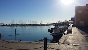 Un puerto deportivo con barcos amarrados, cielo despejado y un edificio que dice "VENTA DE HIELO".