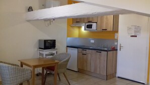 A compact kitchen with a microwave, a sink, and a refrigerator. There is a small dining table with chairs.