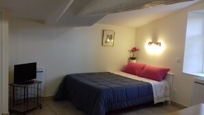 A bedroom with a bed, a TV on a stand, a wall-mounted light, and a framed picture.