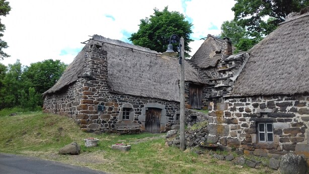 A stone building with a thatched roof, a bell, and a wooden door.