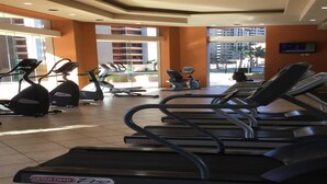 Une salle de sport équipée de plusieurs tapis de course, de vélos d’exercice et d’un écran de télévision.
