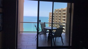Un balcon avec une table et des chaises, donnant sur une étendue d’eau et un bâtiment.