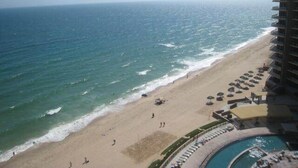 Une vue sur la plage depuis un hôtel de grande hauteur, avec une piscine et des chaises longues.