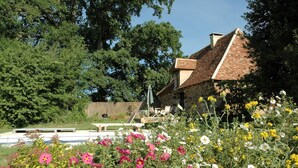 Ein Steinhaus mit einem Ziegeldach, umgeben von üppiger Vegetation und blühenden Pflanzen.