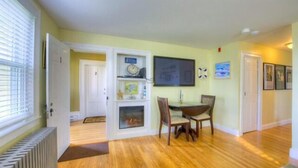 A dining area with a wooden table and chairs, a clock on the wall, and a door leading to another room.
