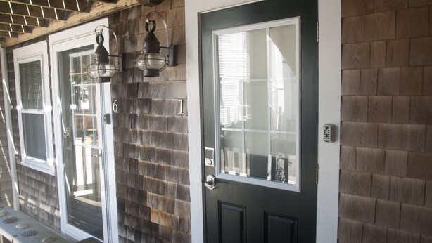 A black door with a glass panel, a wooden wall with a brick pattern, and a metal lantern above the door.