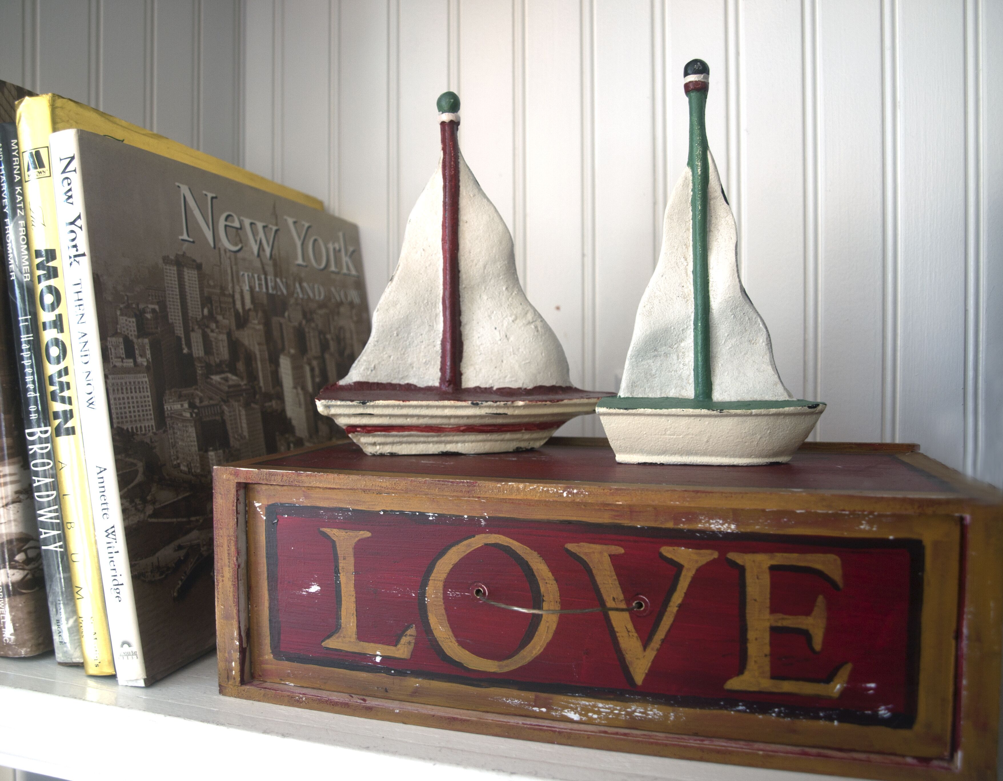 A shelf with books and two small sailboats on a wooden box with the word "LOVE" painted on it.