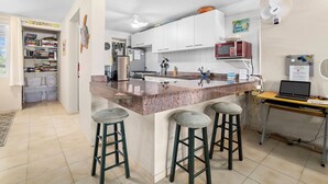 A modern kitchen with a central island, bar stools, a microwave, and a laptop on a desk. - Your Place In Paradise! Just steps to private dive beach and resort pool (Kralendijk)