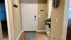 Un couloir avec un plancher en bois, une porte blanche, un petit tapis et une plante sur le côté droit.
