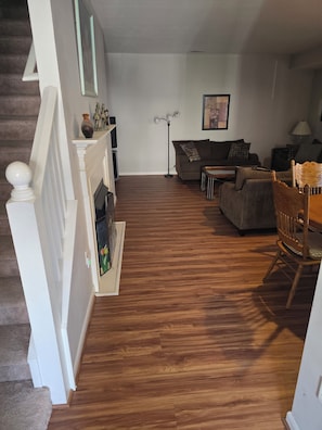 Een woonkamer met een open haard, een bank, een salontafel en een eettafel met stoelen.