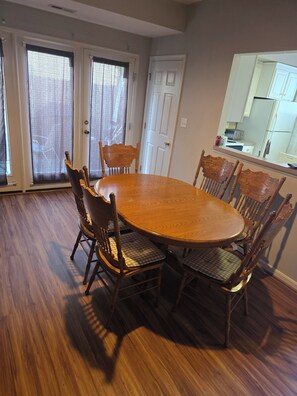 A dining area with a round wooden table surrounded by six chairs, a sliding glass door, and a kitchen area visible through an open door. - Blue Ridge Beauty Home Dog Friendly, Walk to Rivers, A.T. Trail, & HF. NEW LVP (Bolivar)