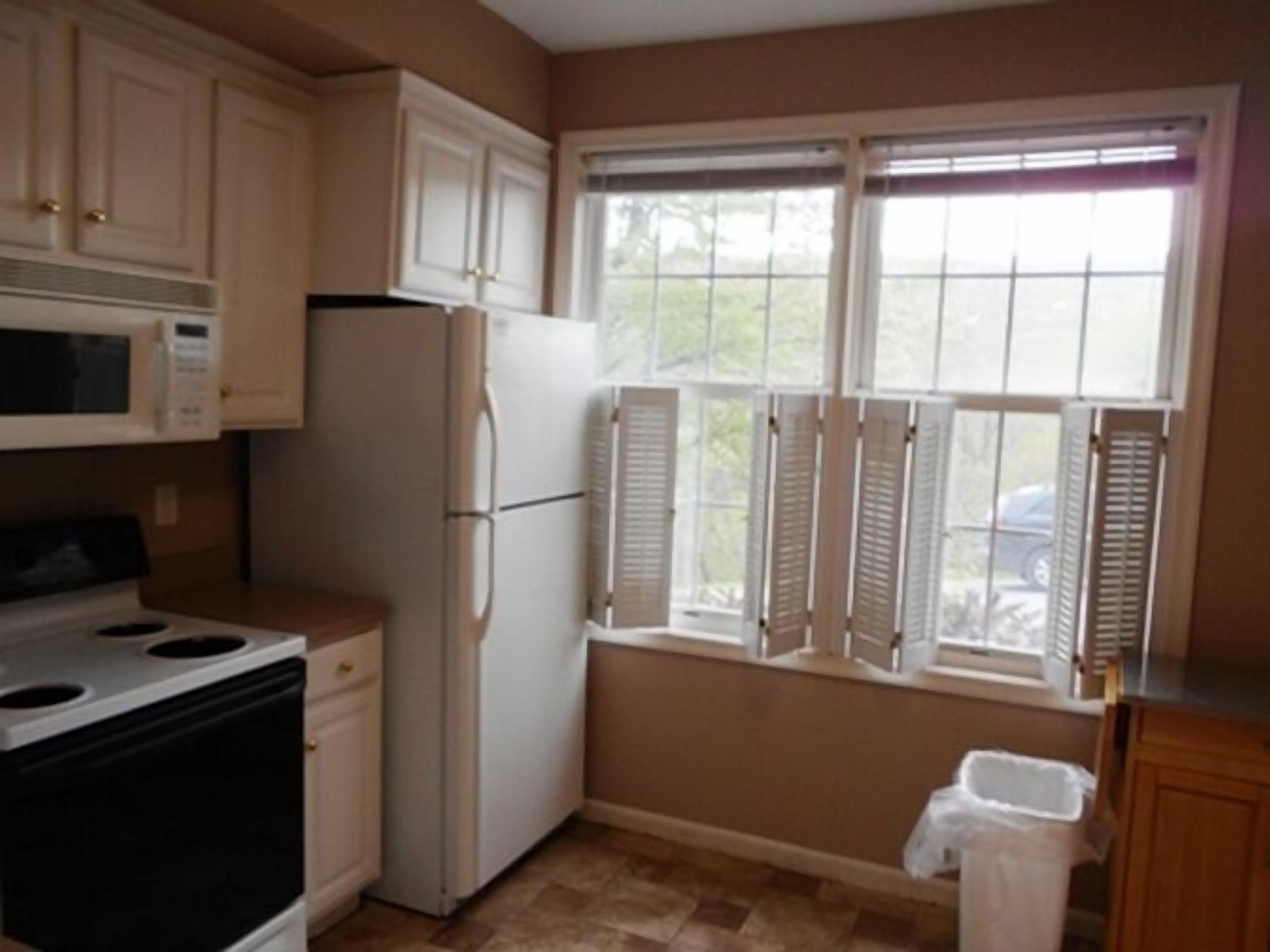A kitchen with white cabinets, a stove, a refrigerator, and a window with shutters.