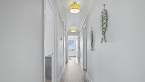 A hallway with a light wooden floor, white walls, and a yellow ceiling light. - Finley House with Beautiful Gulf View (Gulfport)