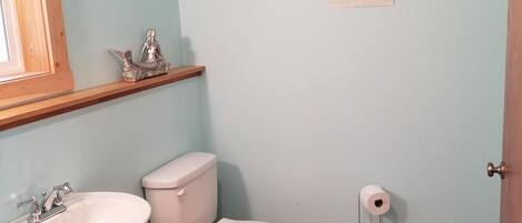 Un baño con lavamanos, inodoro y un estante con objetos decorativos.