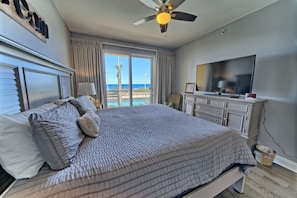 A bedroom with a bed, a TV, a ceiling fan, and a view of the ocean.