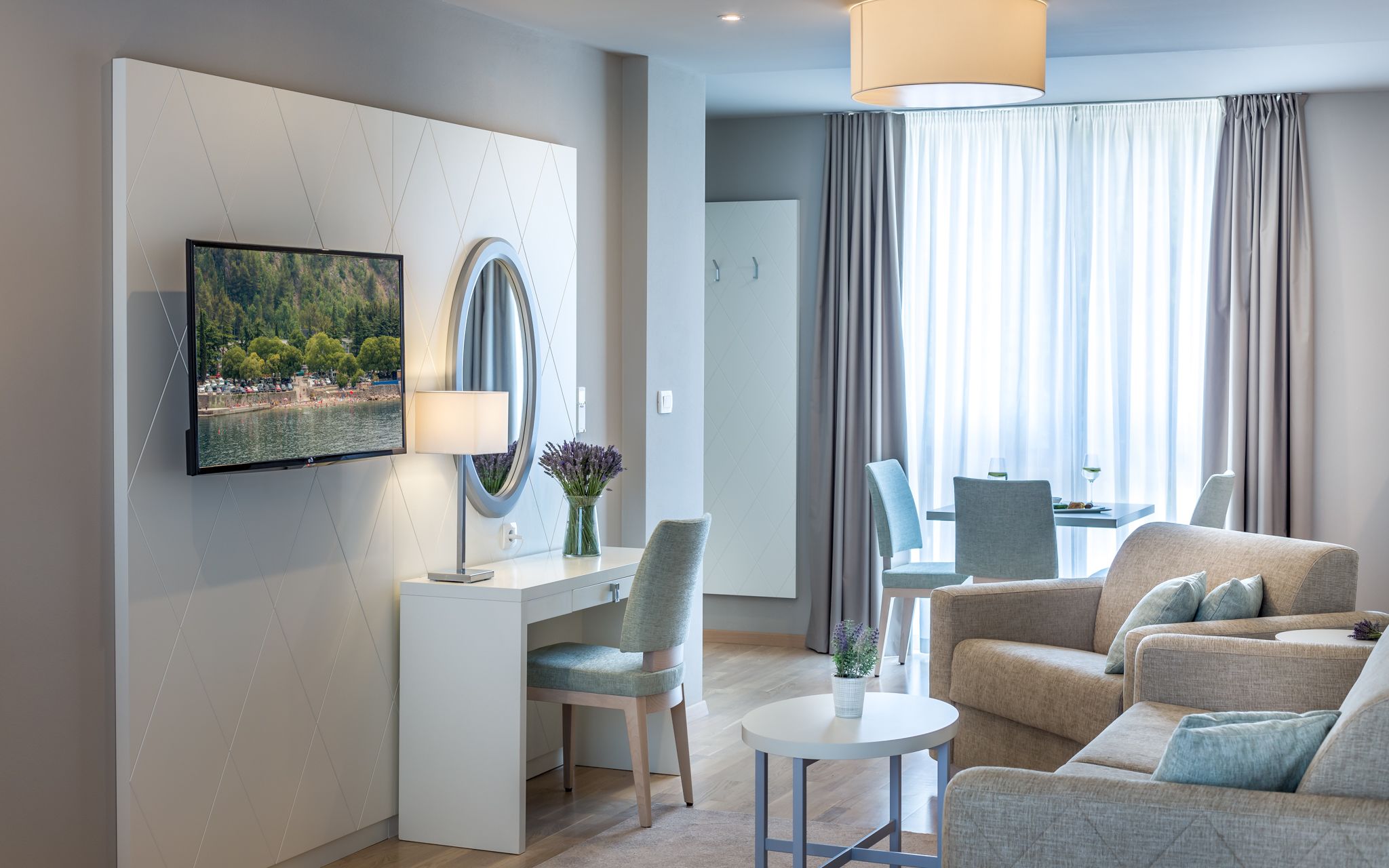 A modern hotel room with a flat-screen TV, a desk with a chair, a sofa, and a dining area with a table and chairs.