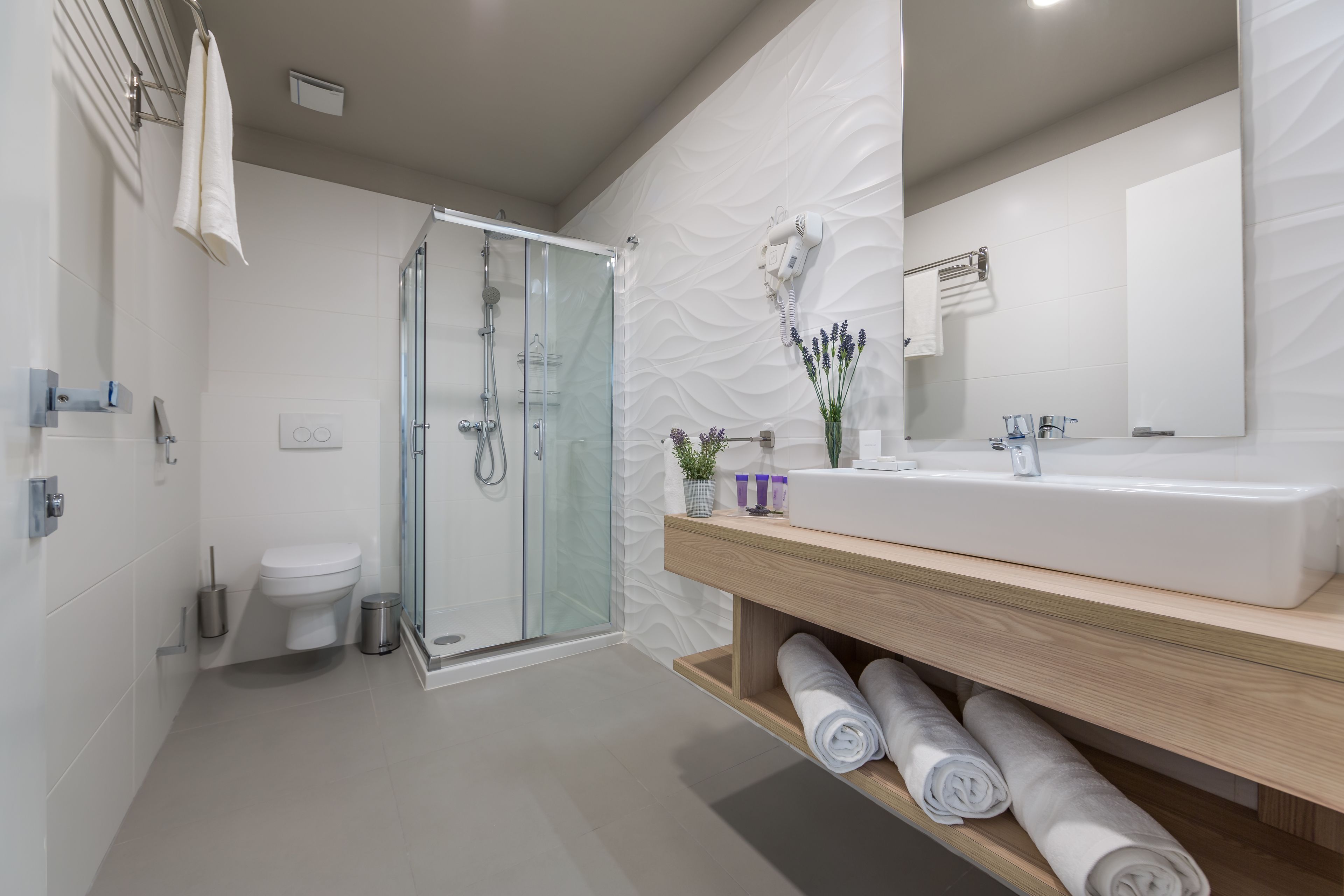 A modern bathroom with a glass shower enclosure, a white sink, and a wooden vanity.