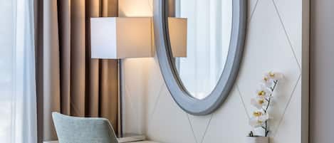Une chambre d’hôtel équipée d’un bureau, d’une chaise, d’un grand miroir, d’une lampe et d’un vase contenant des orchidées.