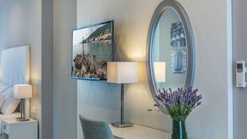 Een moderne hotelkamer met een grote spiegel, een flatscreen televisie, een bedlamp, een stoel en een vaas met lavendelbloemen.