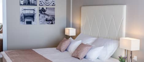 A neatly made bed with white and pink bedding, two bedside lamps, and a small potted plant on the nightstand.