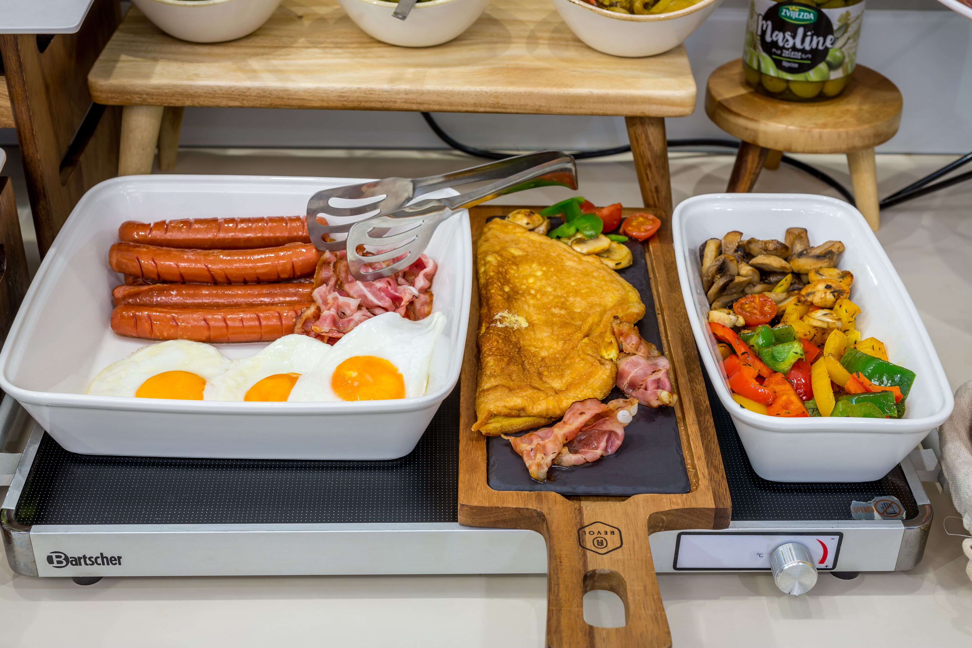 Un buffet de petit-déjeuner comprenant des saucisses, des œufs, une omelette et un plat de légumes.
